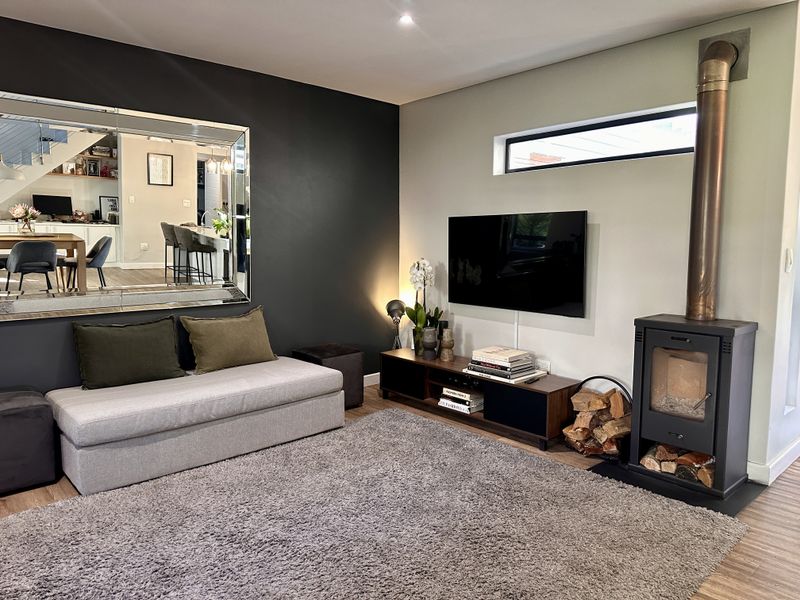 Modern living room featuring a sleek freestanding fireplace, laminate flooring, and a contemporary dark accent wall with a large decorative mirror.