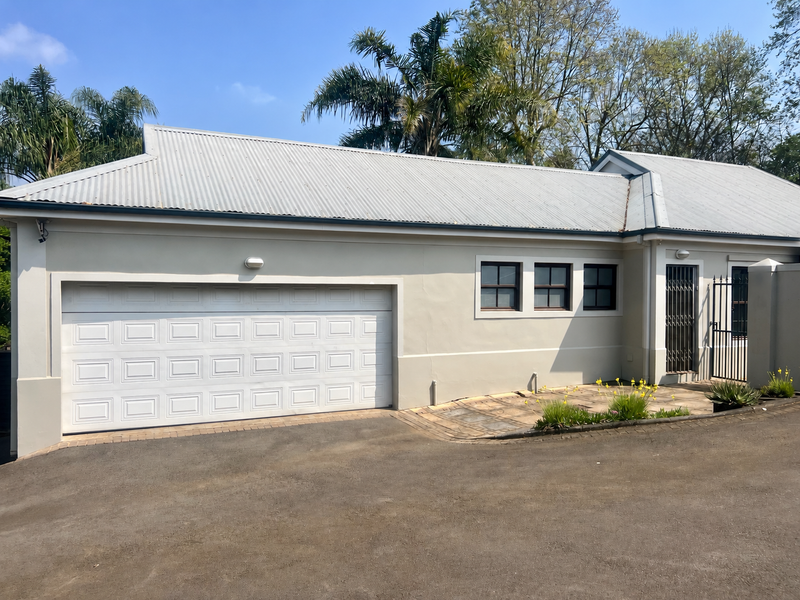 A well-maintained garage exterior featuring a clean sectional door, corrugated metal roofing, and a paved driveway with secure gated access.