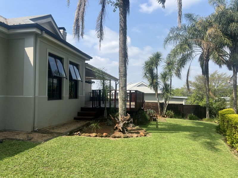 A well-maintained rear exterior view featuring a raised timber deck, landscaped garden, and modern top-hung window frames.