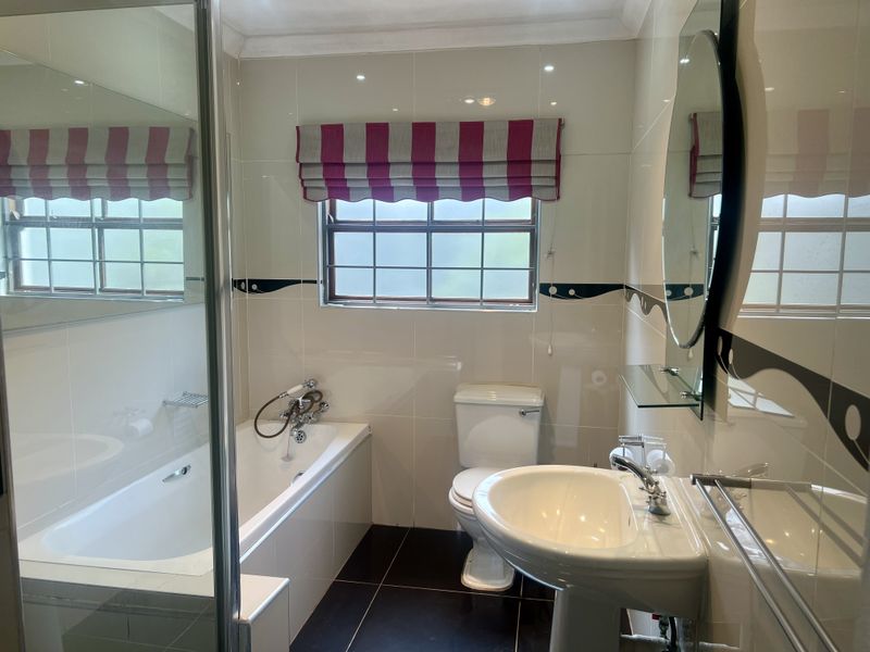 A clean, functional bathroom featuring a bathtub, pedestal sink, toilet, and tiled finishes with a window for natural light.