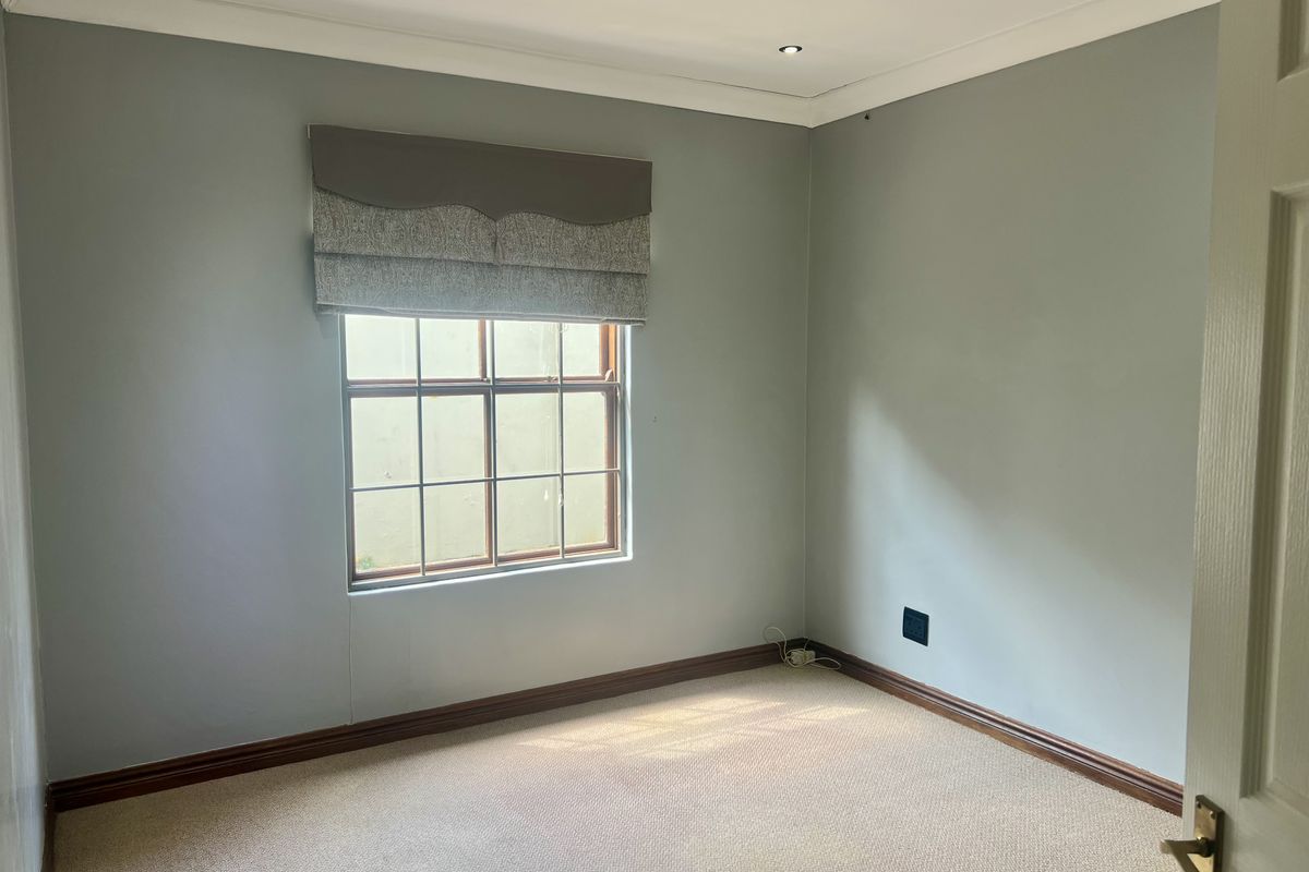 A clean, empty bedroom featuring neutral wall paint, carpeted flooring, recessed downlighting, and a timber-framed window with a fitted pelmet.