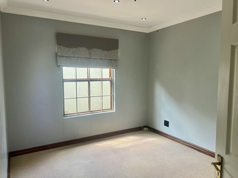 A clean, empty bedroom featuring neutral wall paint, carpeted flooring, recessed downlighting, and a timber-framed window with a fitted pelmet.