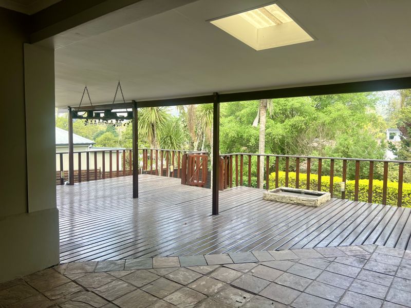 Spacious covered patio featuring timber decking, a built-in fire pit, and a skylight, offering an open outdoor entertainment area with garden views.