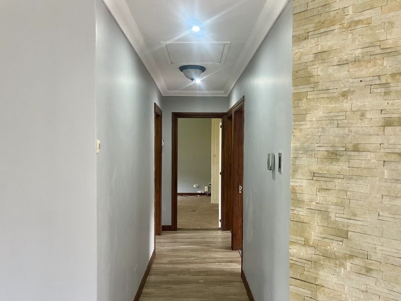 A bright hallway featuring laminate flooring, a textured stone feature wall, and recessed lighting, leading through to an adjacent room.