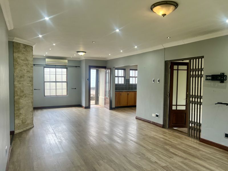 Spacious open-plan living area featuring laminate flooring, a stone-clad feature wall, recessed lighting, and direct access to the kitchen and exterior.