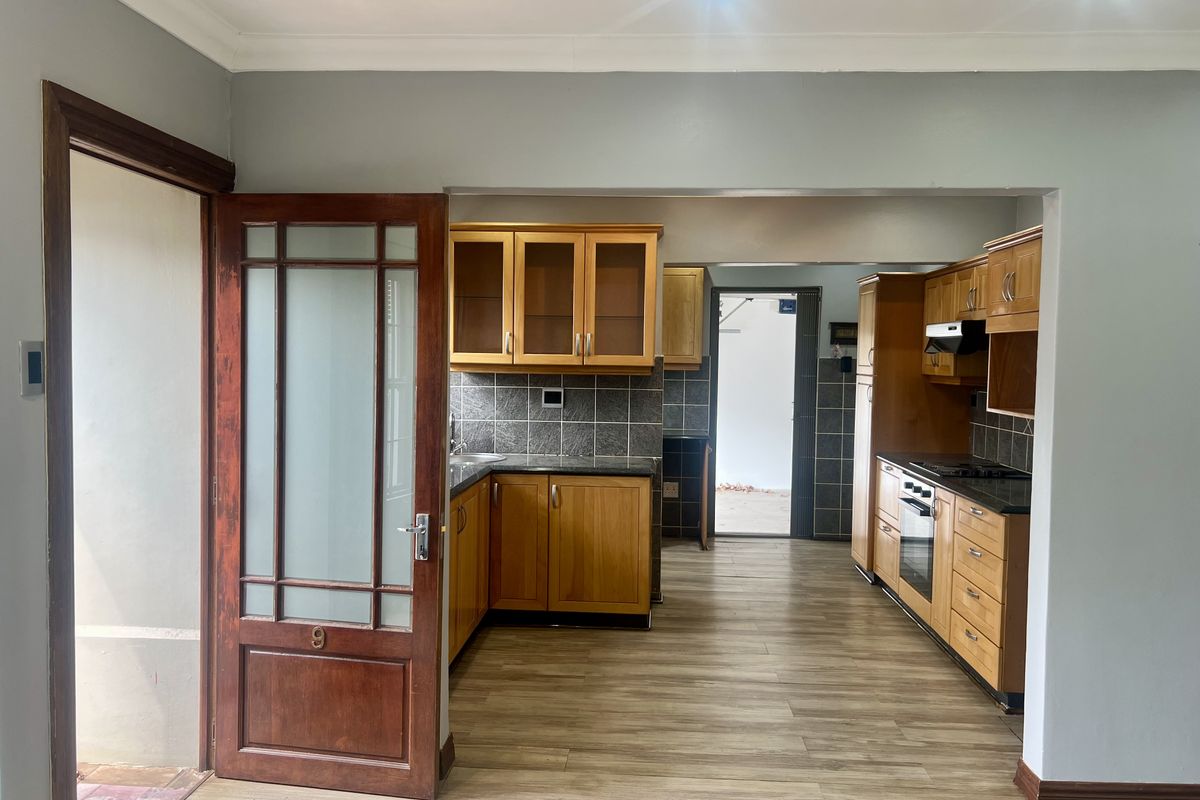 A functional kitchen featuring wooden cabinetry, granite countertops, built-in oven, hob, and extractor fan, with laminate flooring and recessed lighting.
