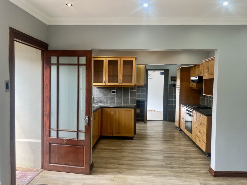 A functional kitchen featuring wooden cabinetry, granite countertops, built-in oven, hob, and extractor fan, with laminate flooring and recessed lighting.