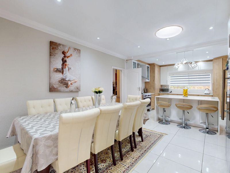 A bright open-plan kitchen and dining area featuring modern cabinetry, a central island with breakfast bar seating, and polished tiled flooring throughout.