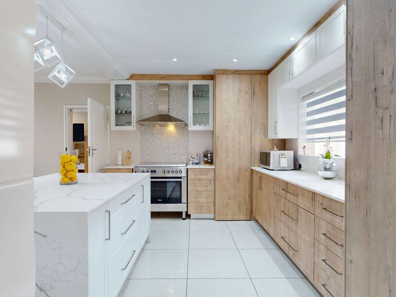 Modern kitchen featuring a central island with quartz countertops, high-end cabinetry, built-in oven, extractor fan, and sleek tiled flooring.