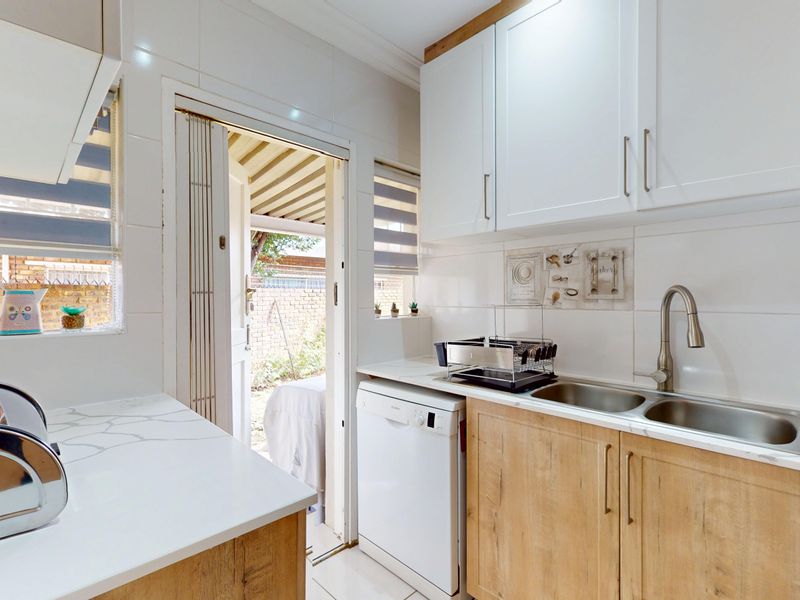 A bright, modern kitchen featuring light wood-finish cabinetry, white countertops, a double sink, and direct access to the outdoor area through a folding door.