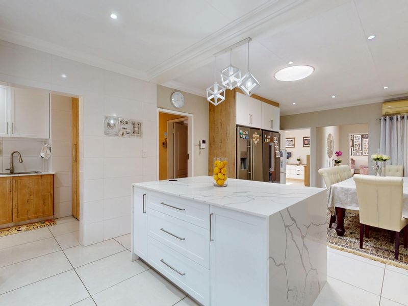 Modern open-plan kitchen featuring a central island with quartz countertops, sleek cabinetry, and an adjacent scullery area, finished with clean tiled flooring.