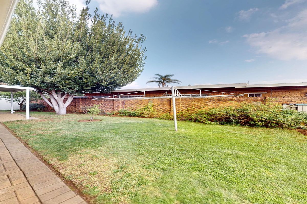 A spacious rear garden featuring a paved patio area, a large lawn, and a brick boundary wall.