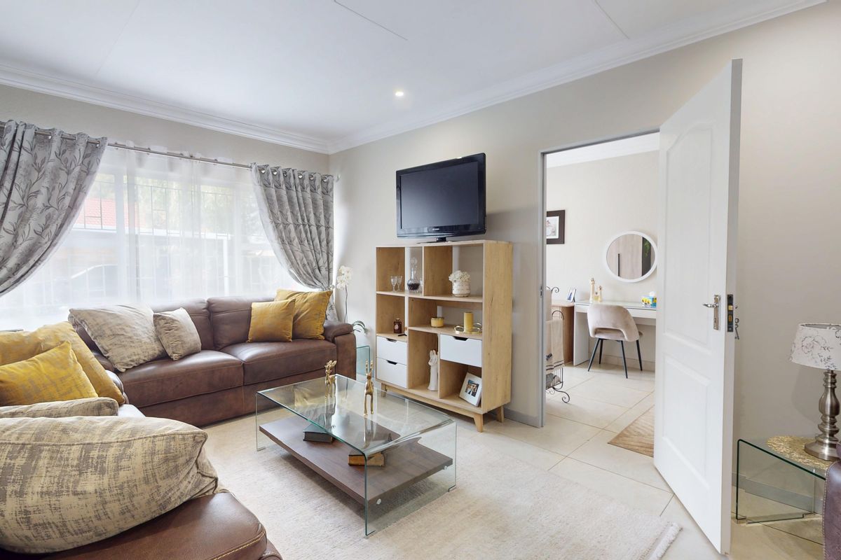 A well-maintained living room featuring tiled flooring, coved ceilings, and recessed lighting, with an open doorway leading to an adjacent room.
