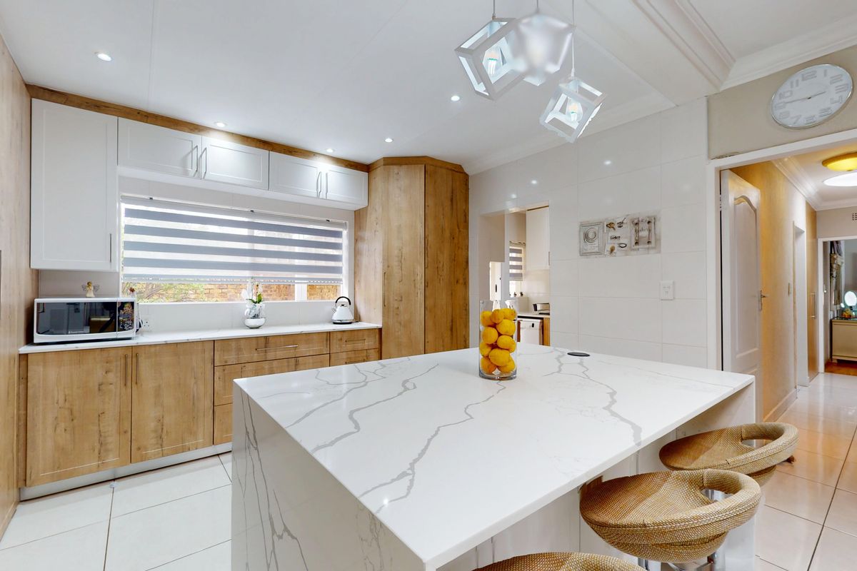 Modern kitchen featuring a large quartz island, sleek wood-tone and white cabinetry, recessed lighting, and high-quality tiled flooring.