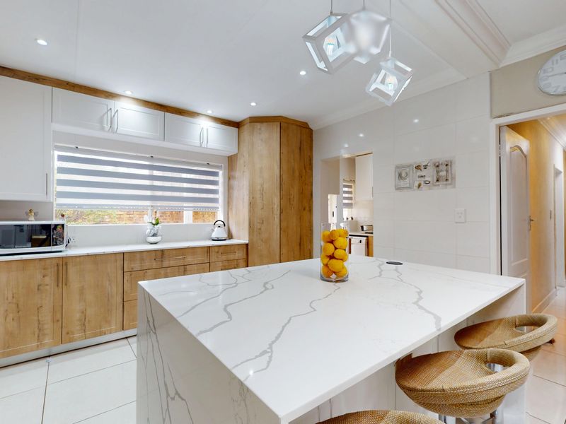 Modern kitchen featuring a large quartz island, sleek wood-tone and white cabinetry, recessed lighting, and high-quality tiled flooring.