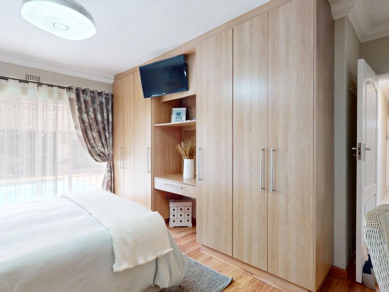 A well-maintained bedroom featuring extensive light wood built-in cupboards with an integrated vanity area and warm wooden flooring.