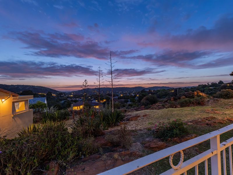 A scenic twilight view overlooking a suburban landscape with rolling hills, captured from a residential balcony with exterior lighting.