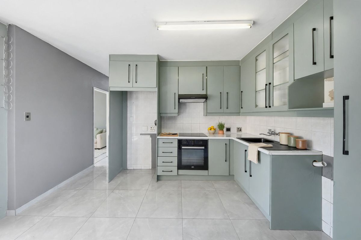 A modern kitchen featuring sage green cabinetry, built-in oven and hob, tiled backsplash, and neutral floor tiles, offering a clean and functional workspace.