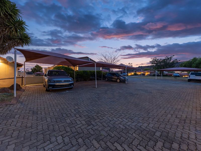 A paved communal parking area featuring multiple shade cloth carports at dusk.
