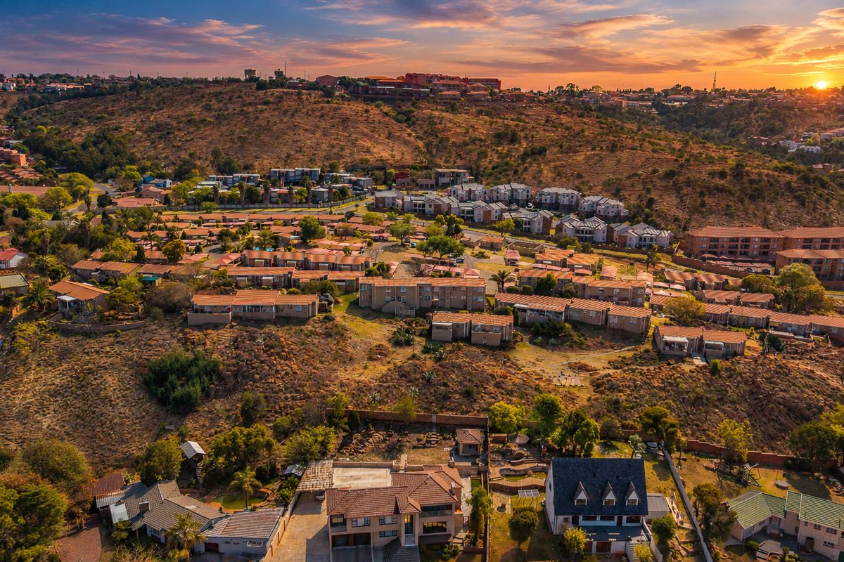 An expansive aerial view of a residential townhouse estate set within a hilly landscape at sunset.