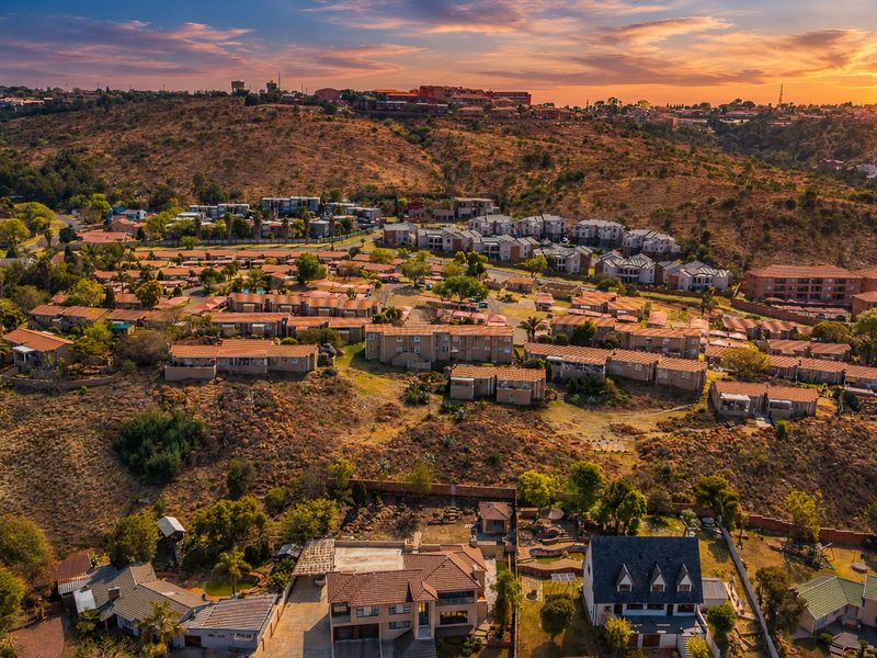 An expansive aerial view of a residential townhouse estate set within a hilly landscape at sunset.