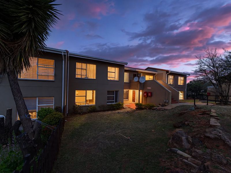 Rear elevation of a multi-unit townhouse complex at dusk, featuring a shared garden area, paved pathways, and exterior lighting.