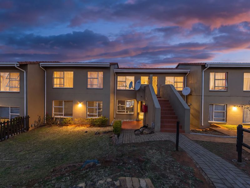 A rear view of a multi-unit townhouse complex at dusk, featuring a central concrete staircase, paved pathways, and exterior lighting.