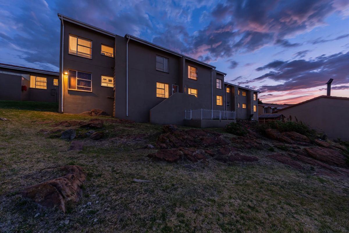 Rear elevation of the townhouse complex at dusk, featuring multi-level residential units with exterior lighting and landscaped rocky terrain.