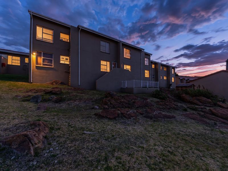 Rear elevation of the townhouse complex at dusk, featuring multi-level residential units with exterior lighting and landscaped rocky terrain.