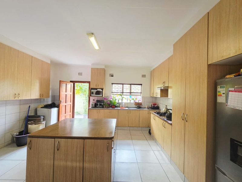 A functional kitchen featuring light wood-finish cabinetry, a central island, tiled flooring, and a built-in hob with an extractor fan.