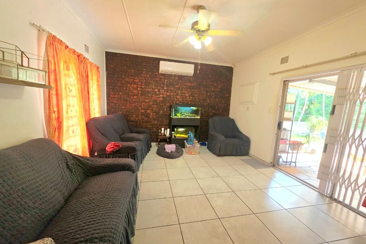 A living room featuring an exposed brick accent wall, ceramic tiled flooring, a ceiling fan, and sliding glass doors leading to the patio.