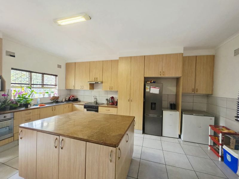 Spacious kitchen featuring light wood cabinetry, a central island with stone countertop, tiled backsplash, and integrated appliances.