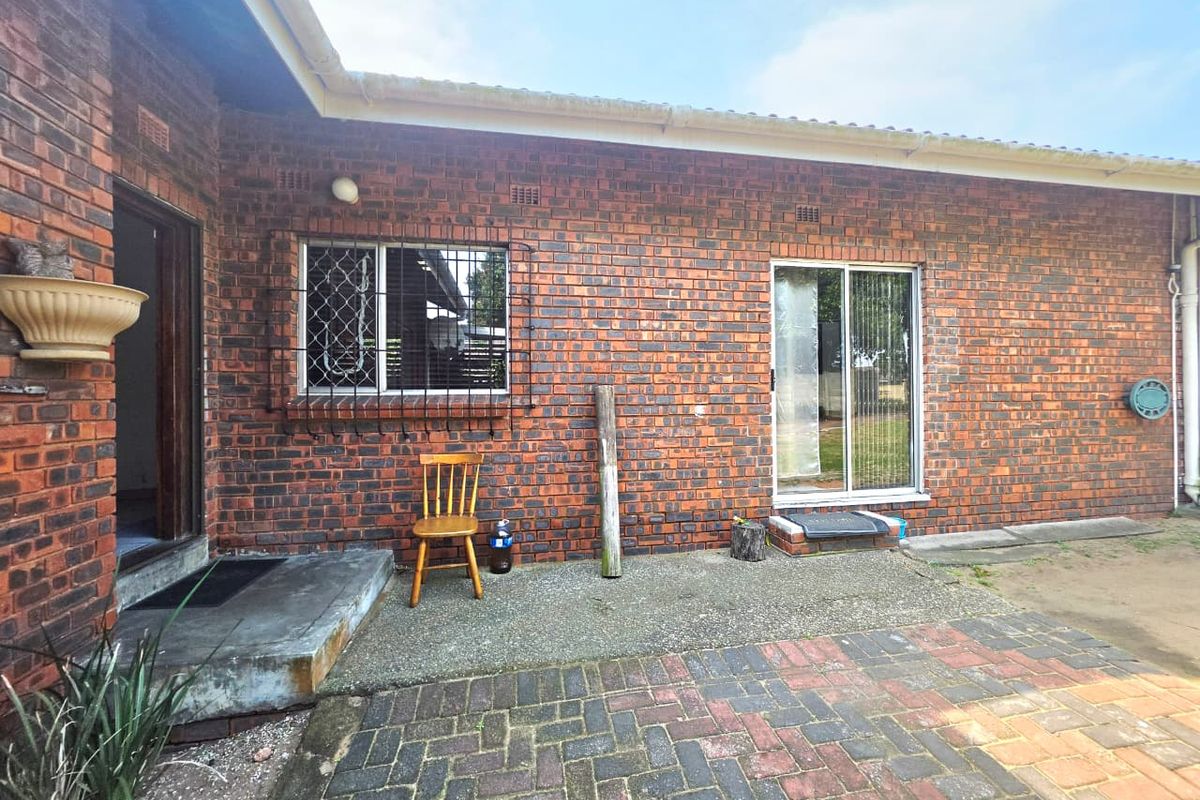 Rear exterior view of the house featuring a face brick facade, paved patio area, and sliding glass door access.