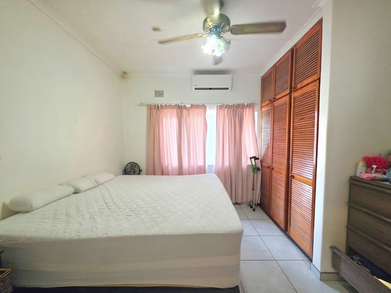 A bedroom featuring tiled flooring, built-in wooden louvered wardrobes, a ceiling fan, and a wall-mounted split-system air conditioner.