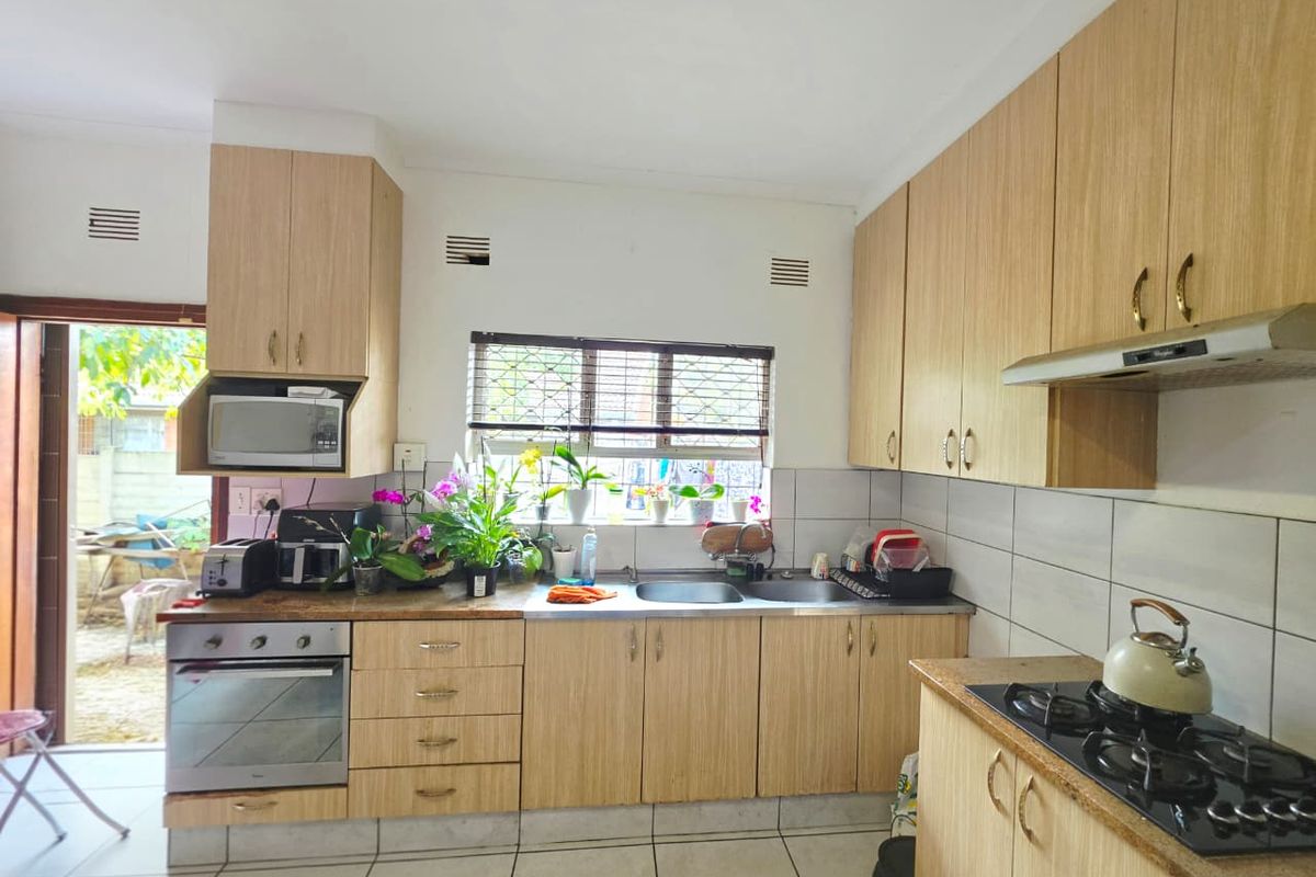 Functional kitchen featuring light wood-finish cabinetry, laminate countertops, a gas hob with extractor, and direct access to the outdoor area.