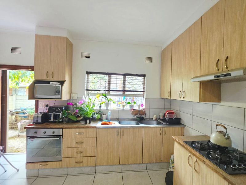 Functional kitchen featuring light wood-finish cabinetry, laminate countertops, a gas hob with extractor, and direct access to the outdoor area.