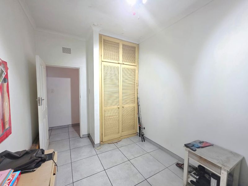 A simple bedroom featuring tiled flooring and a built-in cupboard with louvered doors, requiring minor cosmetic updates.