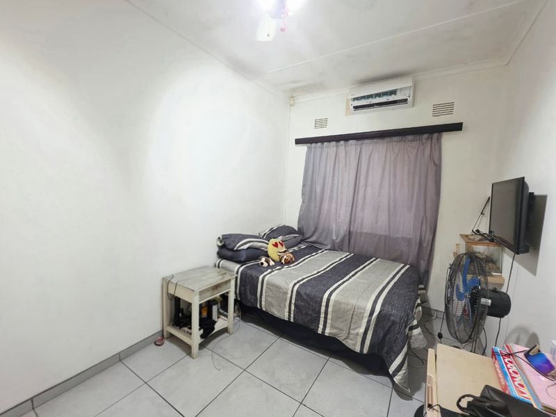 A compact bedroom featuring tiled flooring and a wall-mounted air conditioning unit, showing signs of ceiling water damage.