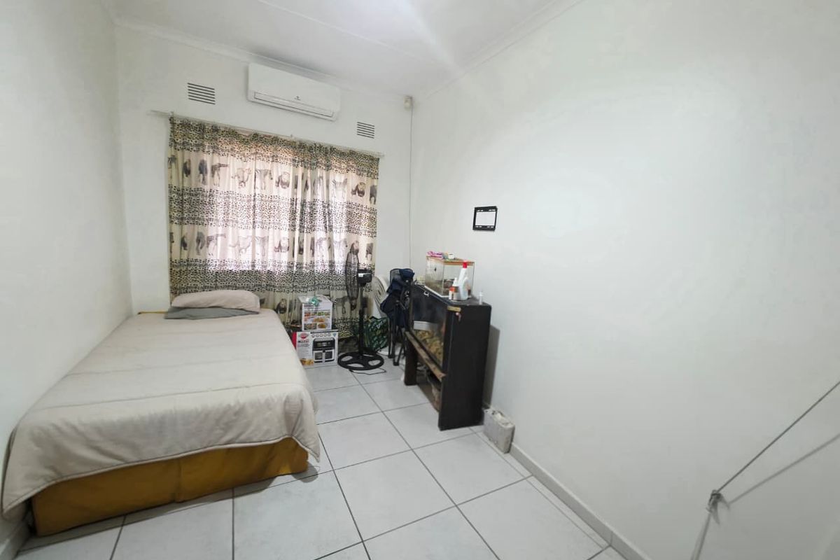 A functional bedroom featuring tiled flooring, neutral walls, and a wall-mounted split-system air conditioner for climate control.