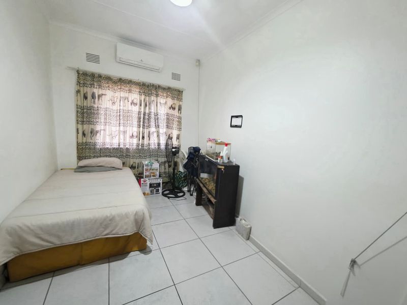A functional bedroom featuring tiled flooring, neutral walls, and a wall-mounted split-system air conditioner for climate control.
