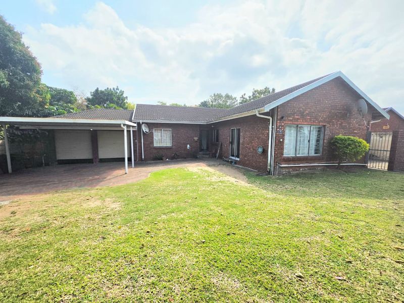 A single-story brick house featuring a tiled roof, a double carport, and a paved driveway set within a spacious front garden.
