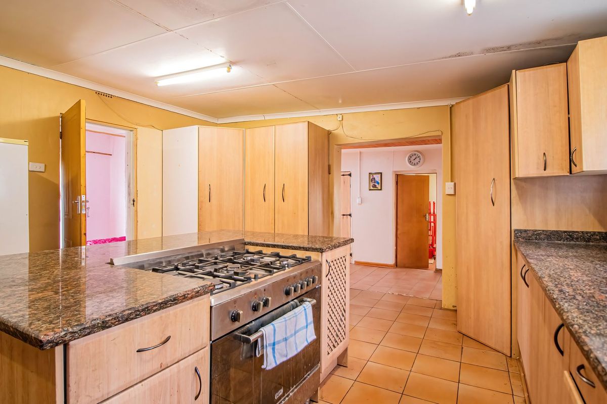 A functional kitchen featuring granite countertops, built-in wooden cabinetry, and a gas stove, with tiled flooring and direct access to adjacent living areas.