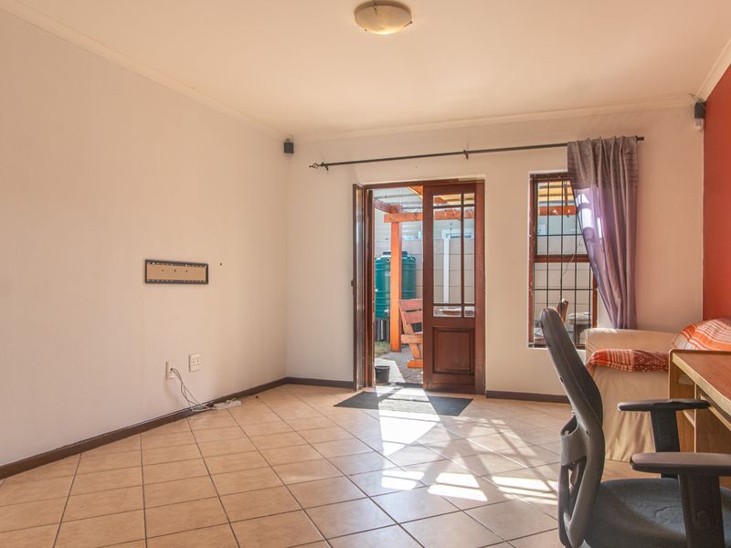 A living room featuring tiled flooring, a timber door with security gate leading to an outdoor area, and a feature wall.
