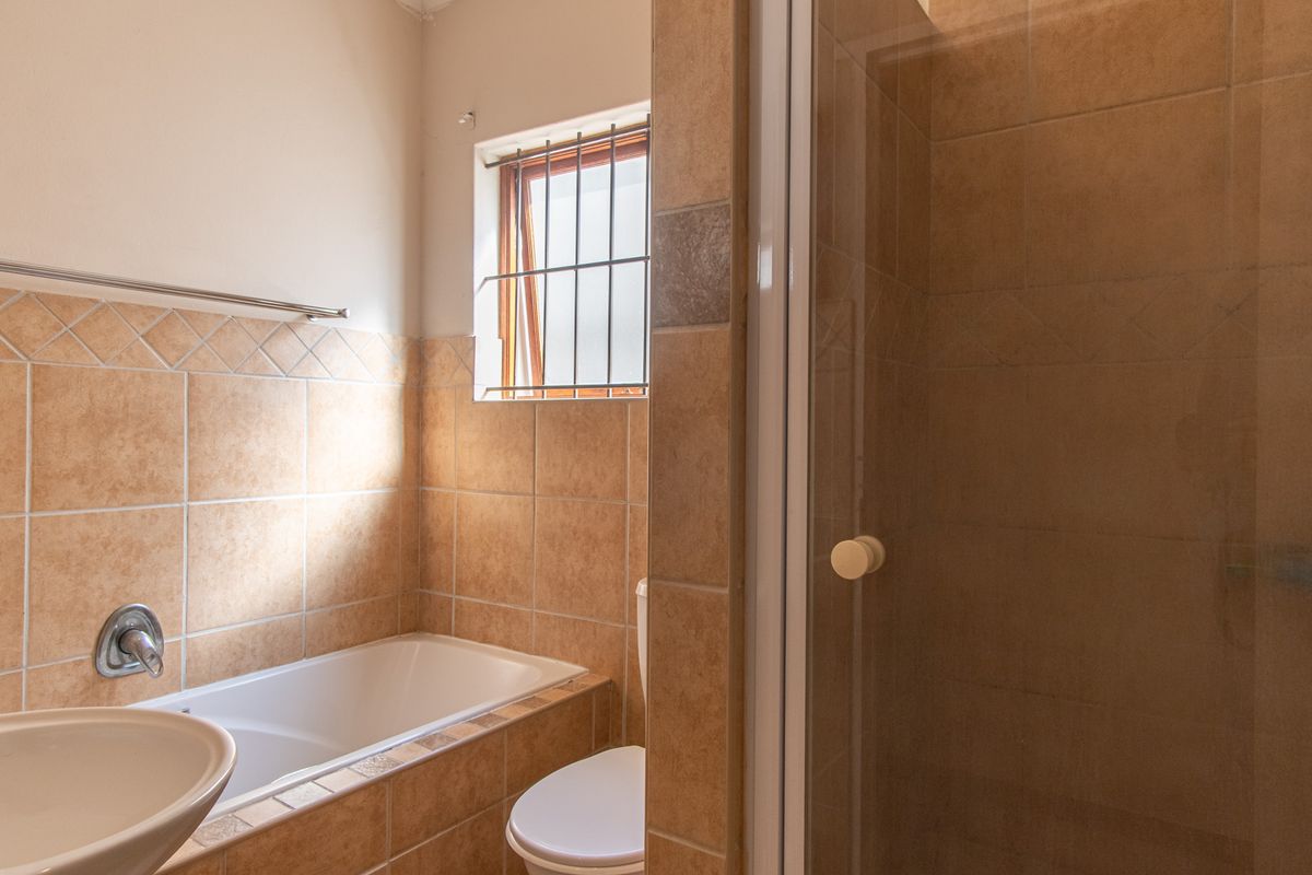 A functional bathroom featuring a built-in bathtub, separate shower enclosure, and neutral wall tiling with a window for natural light.