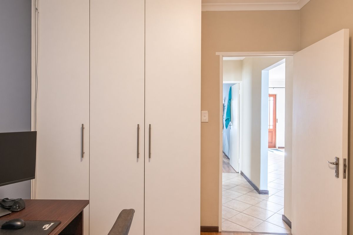 A bedroom featuring built-in cupboards and tiled flooring, with a view through the doorway into the connecting hallway.