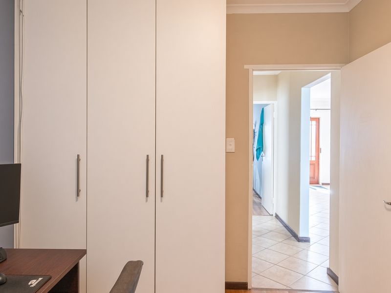 A bedroom featuring built-in cupboards and tiled flooring, with a view through the doorway into the connecting hallway.