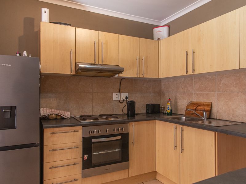 A functional kitchen featuring light wood-finish cabinetry, a built-in oven with electric hob, extractor fan, and a tiled splashback with a stainless steel sink.