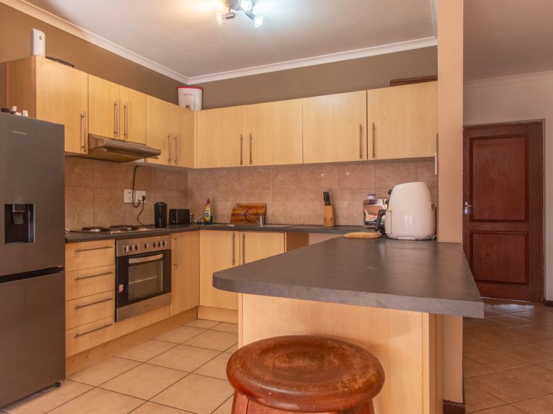 A functional kitchen featuring light wood cabinetry, dark laminate countertops, a breakfast bar, and tiled flooring, providing a practical layout for daily use.