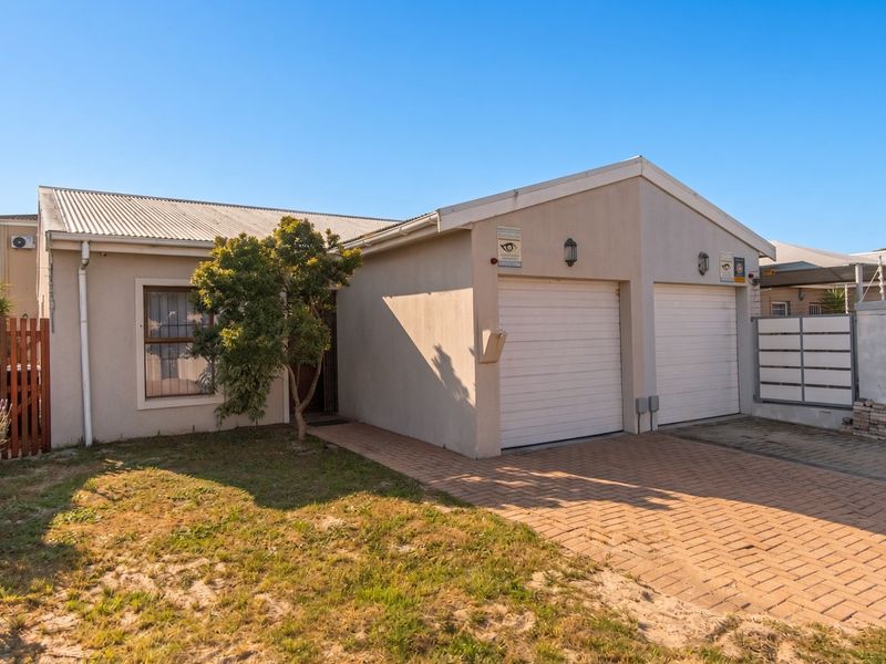 Front view of a townhouse featuring a double garage, paved driveway, and secure perimeter fencing with a small front garden area.