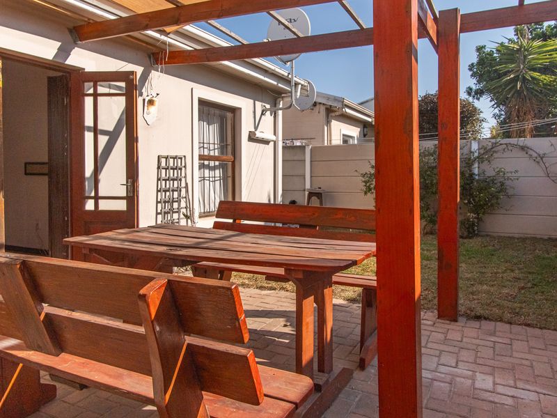 A paved outdoor patio area featuring a timber pergola structure, providing a functional space for outdoor dining and relaxation in the rear garden.